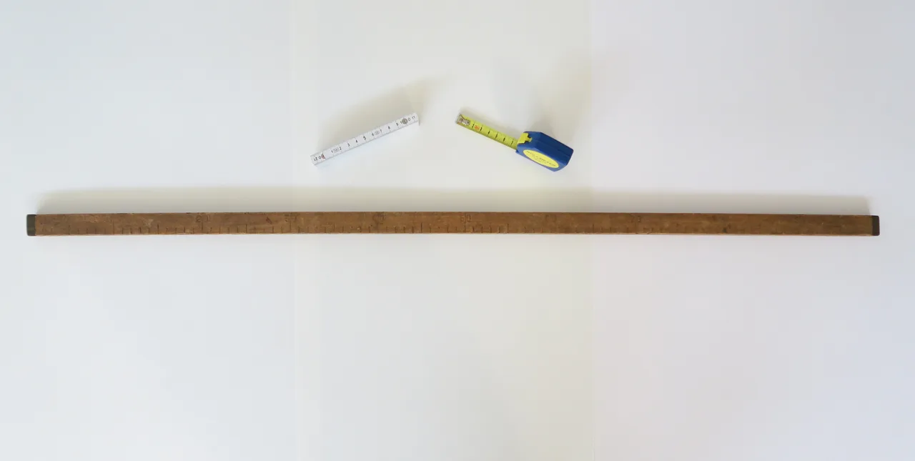 An Austrian metre stick with a centimetre scale, beside a folded rule and a retractable tape