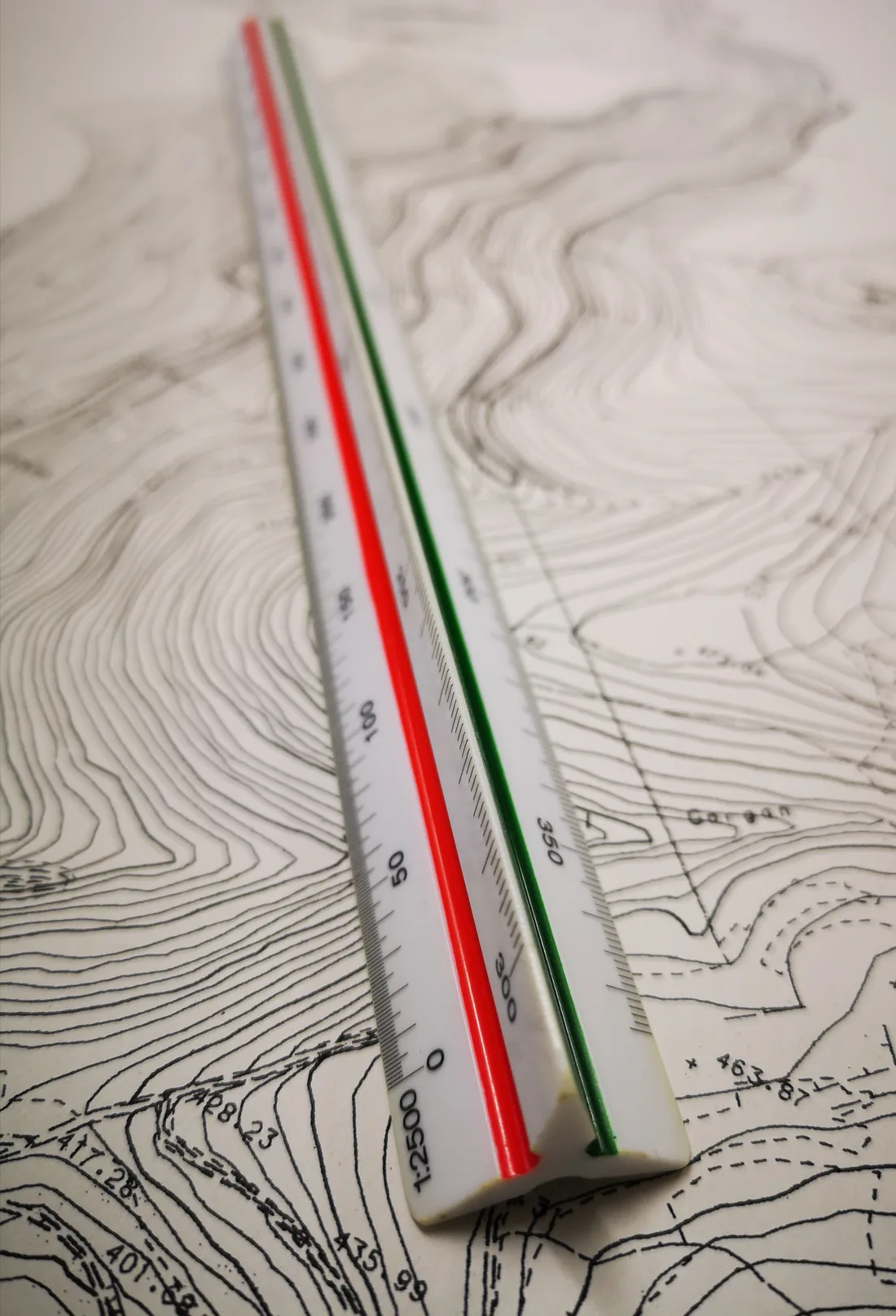A triangular scale ruler marked 1:2500 lying on a contour survey drawing