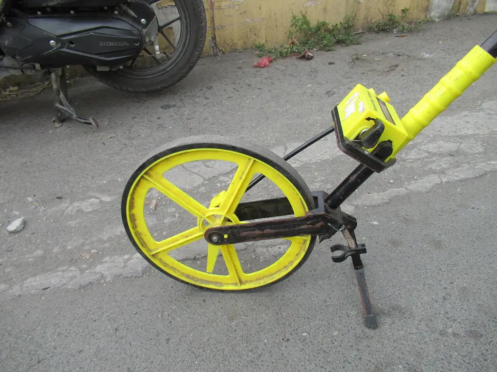 A yellow measuring wheel with a counter, lying on tarmac