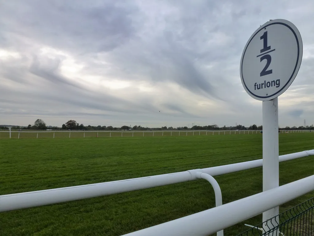 A round sign reading 1/2 furlong on a post beside a racecourse