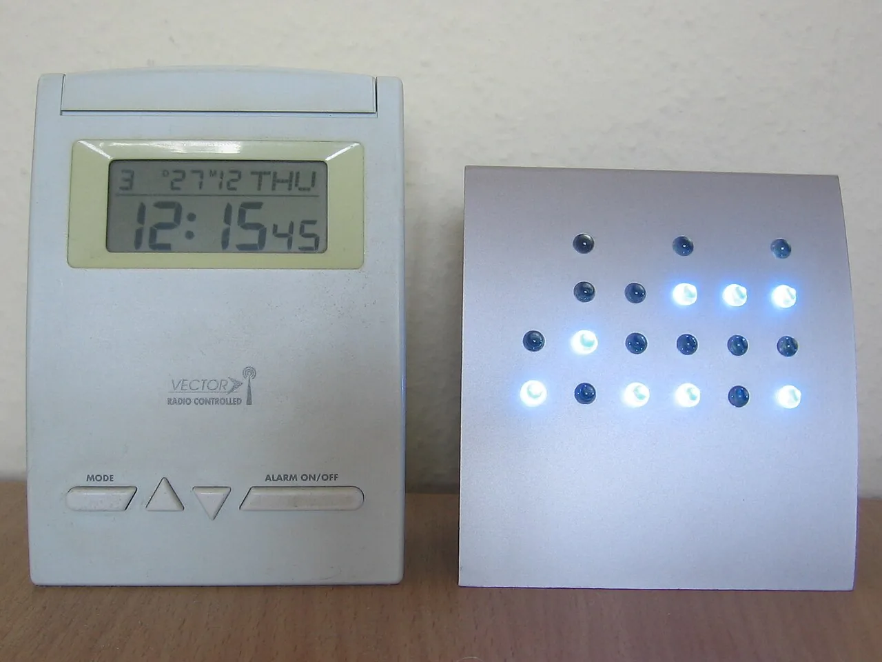 Two clocks side by side: one shows 12:15:45 in digits, the other in rows of lit and unlit lamps