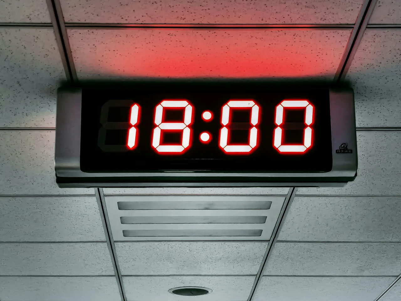 A digital clock hanging from the ceiling, its display showing 18:00