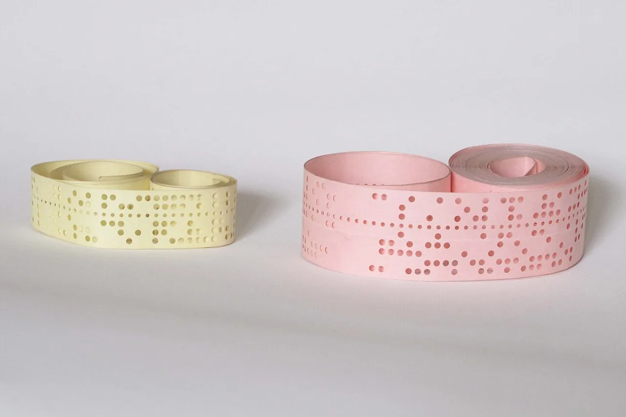 Two coiled paper tapes with rows of punched holes